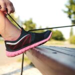 A woman laces her sneakers on a park bench, preparing for a run outdoors.